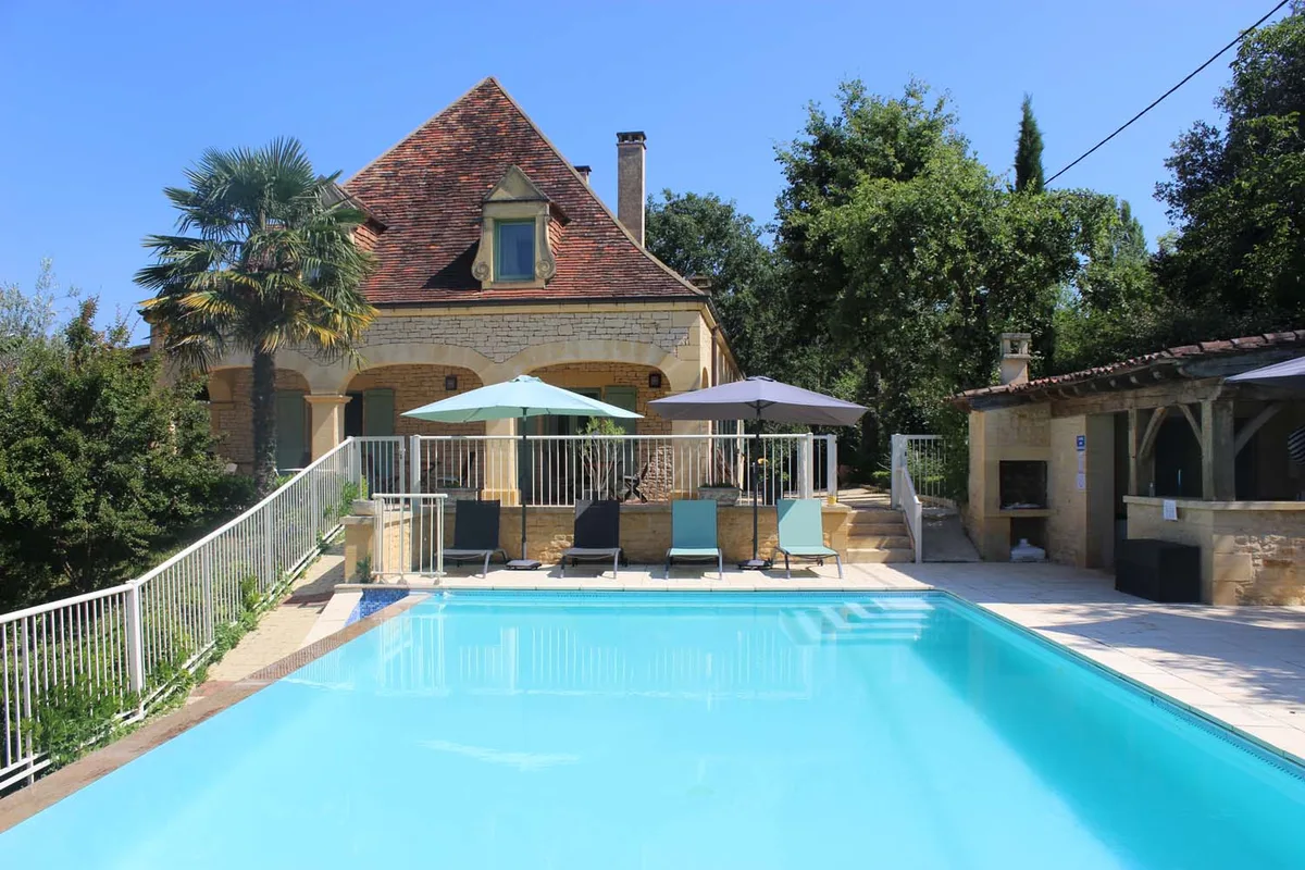 La bâtisse de l’Hôtel Bon Encontre vue depuis la piscine, parasols et transats au bord de l’eau
